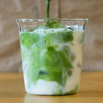 Green matcha liquid being poured into a glass with white foam on a wooden surface